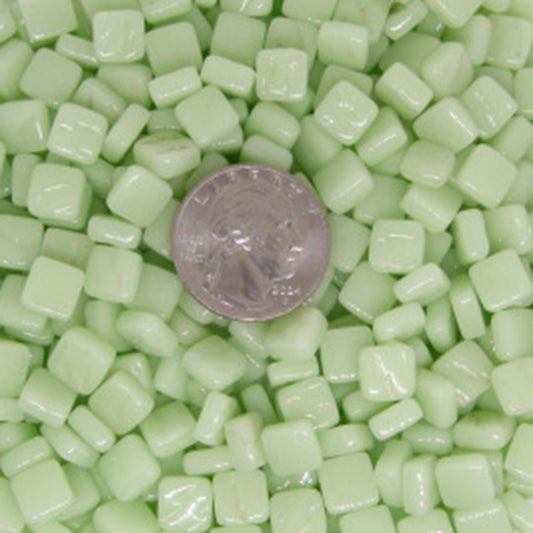 Pastel green 8mm mosaic glass tiles arranged with a quarter for size reference, showcasing vibrant color and glossy finish, ideal for artistic projects.
