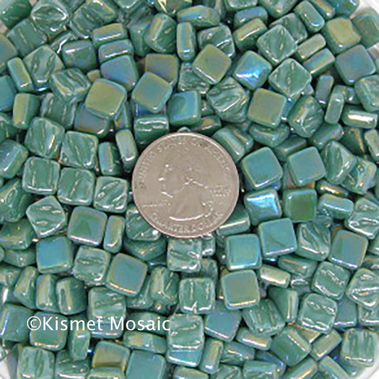 15-i Teal Green 8mm mosaic tiles arranged with a quarter for scale, showcasing vibrant colors and iridescent finish, representing Kismet Mosaic's collection for artists and DIY projects.