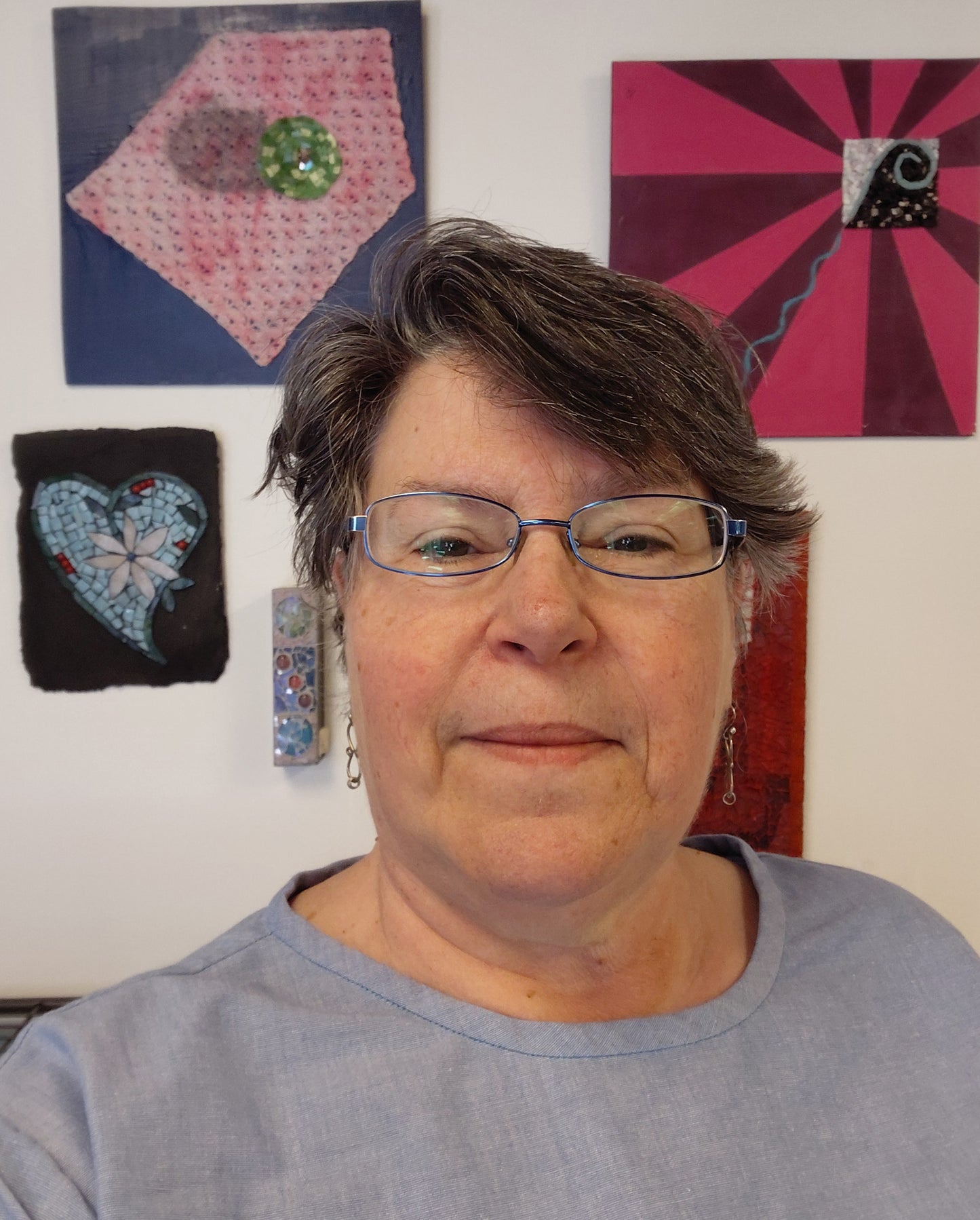 headshot of Kismet Mosaic owner Juanita Canzoneri in front of several of her mosaic art pieces.