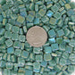 15-i Teal Green 8mm mosaic tiles arranged with a quarter for scale, showcasing vibrant colors and iridescent finish, representing Kismet Mosaic's collection for artists and DIY projects.
