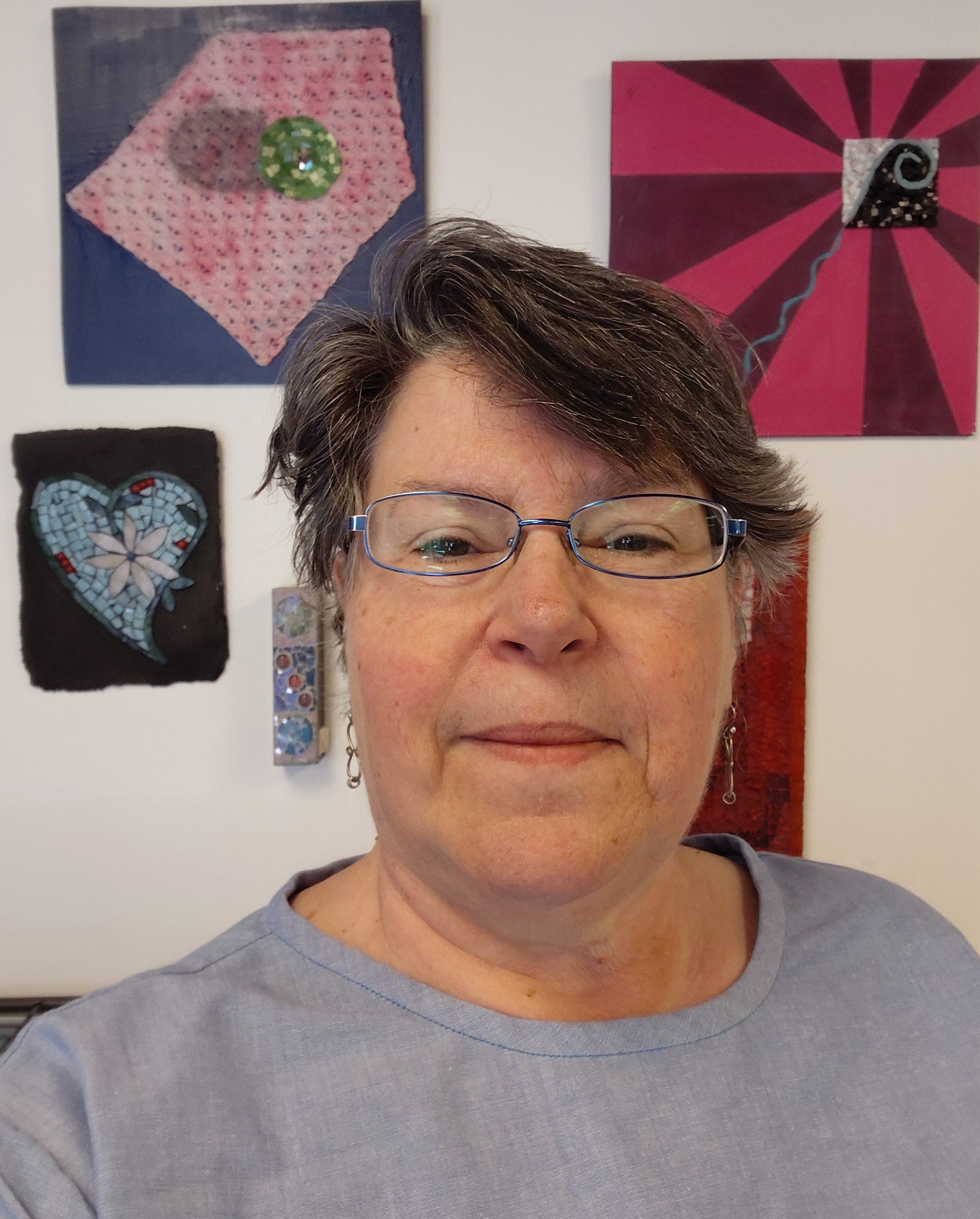 headshot of Kismet Mosaic owner Juanita Canzoneri in front of several of her mosaic art pieces.