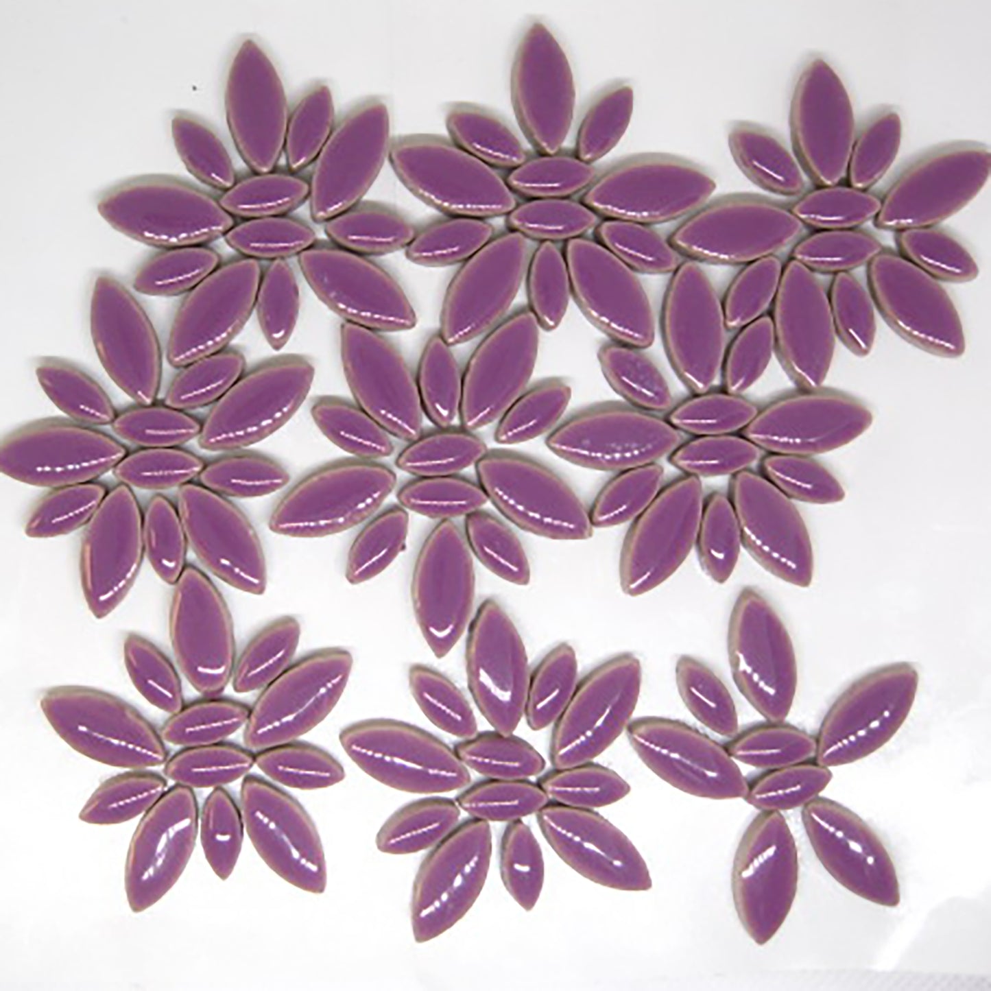 Glazed ceramic petal mosaic tiles in rich purple color arranged in decorative patterns. The tiles feature an elongated petal or ellipse shape in a mix of two sizes - larger oval petals and smaller accent pieces. The deep purple glaze has a glossy, reflective finish that creates beautiful light reflections. This image shows an average tile mix for our 4 ounce quantity.